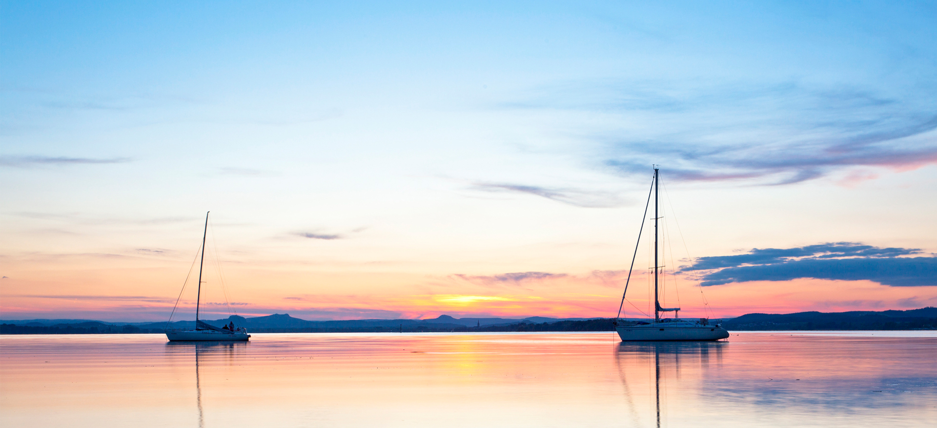 Zwei Segelschiffe auf dem Bodensee im Sonnenuntergang.